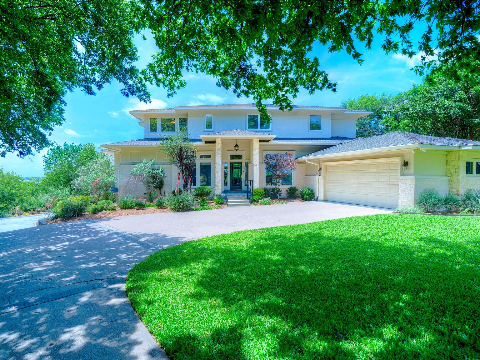 Front elevation of 1132 Mallard Pointe Drive: a two-story transitional home with stone and stucco facade, central front door framed by curved entry landscaping, two attached garage bays on the right.