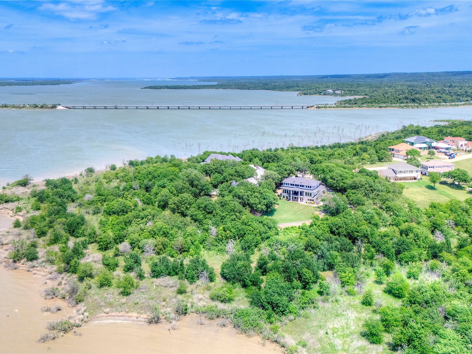 Cinematic wide aerial of the property showing the full extent of the wooded acreage, Joe Pool Lake stretching to the horizon, and the lake bridge crossing the upper portion of the frame.